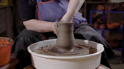 Close up shot of a professional female potter at wheel in studio shaping clay.