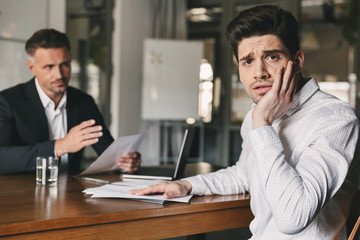 Business, career and placement concept - stressed nervous man worrying during job interview in office, while negotiating with caucasian businessman or director