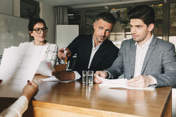 Business, career and placement concept - three executive directors or head managers sitting at table in office, and interviewing woman for teamwork in company - obrazy, fototapety, plakaty
