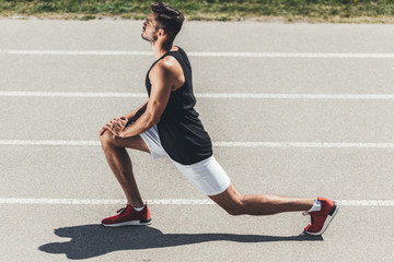 side view of male jogger stretching on running track at sport playground