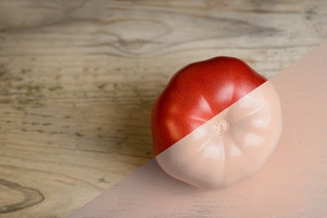 Natural red and beige or ecru half painted tomato on wooden background.