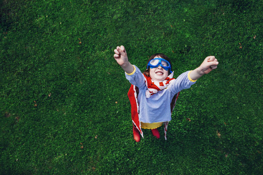Overhead view of a Girl wearing a superhero costume with goggles standing in the garden with her arms in the air