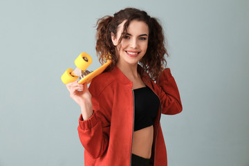 Stylish young woman in casual clothes and with skateboard on color background