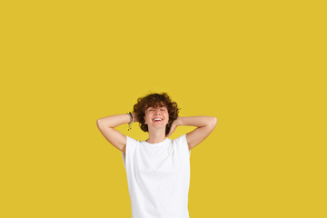 Fototapeta na wymiar Сoncept dizzying success. Young wonderful girl keeps herself for curly head, rejoices in her youth, has great good mood. Copy space, yellow studio background. Happy joyful female student smiling