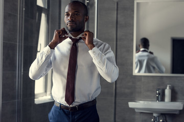 happy young businessman in white shirt putting on his tie at bathroom