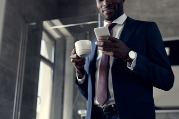 bottom view of handsome young businessman with cup of coffee using smartphone in bathroom