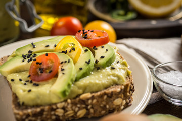 Avocado Spread and Slices with Cherry Tomato and Black Sesame on Wooden Background as Vegetarian Food Concept