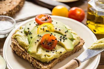 Avocado Spread and Slices with Cherry Tomato and Black Sesame on Wooden Background as Vegetarian Food Concept