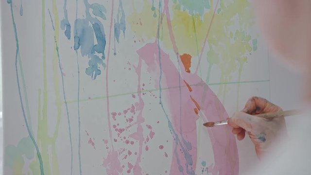 Painter's hand drawing picture with watercolor paints. Using brush and white canvas. Having hand blurred with colorful paint. Working at art atelier. Saturated colors.