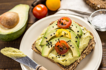 Avocado Spread and Slices with Cherry Tomato and Black Sesame on Wooden Background as Vegetarian Food Concept