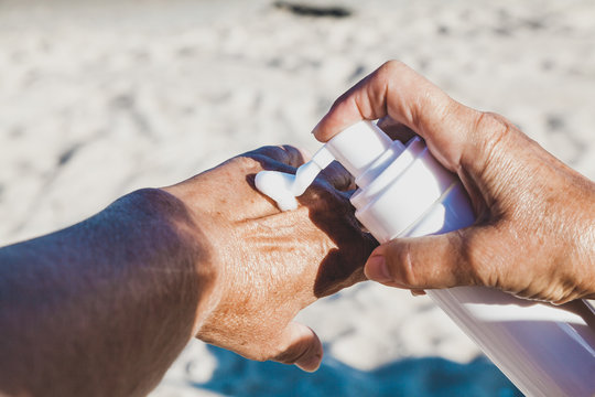 Elderly woman using cream for hand on the beach