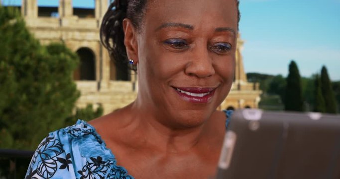 Happy mature black woman using technology near Coliseum, African American woman tourist uses wireless tablet on vacation, 4k