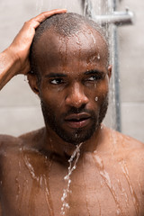 Fototapeta na wymiar close-up view of young african american man washing in shower and looking away