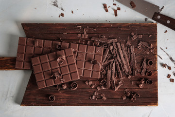 Wooden board with pieces of chocolate on light background