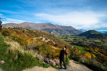 A man taking a photo of a beautiful road between Queenstown and Wanaka via Crown range. Grassland autumn trees with beautiful landscape of rocky mountains.
