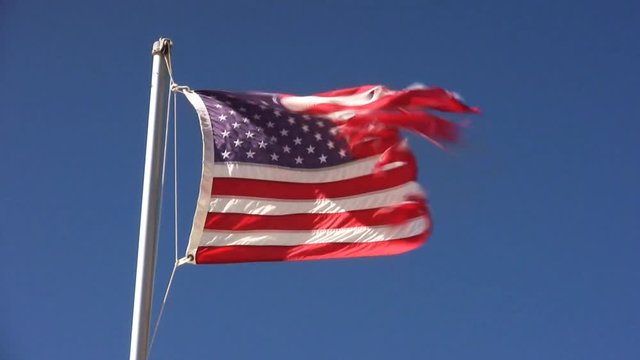 long shot of waving weathered, ragged national flag of the USA in front of blue sky, symbol of politics and political apathy