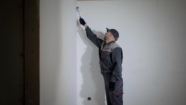 Working man is priming wall in flat.