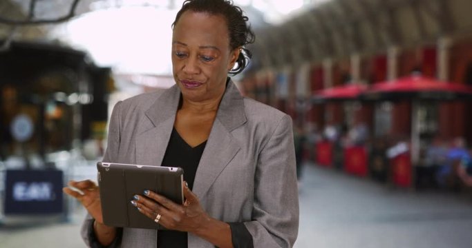 Mature woman using digital tablet and talking to camera outdoors, Happy African American businesswoman uses wireless technology near restaurant, 4k