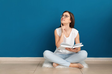 Fototapeta na wymiar Young woman reading book on floor near color wall