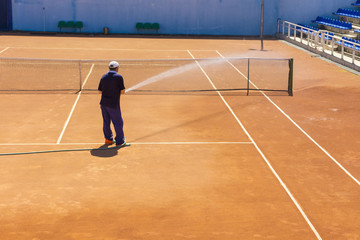 Preparation of a tennis court watering from a hose. A man watering a tennis court