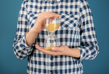 Woman holding hourglass on color background. Time management concept