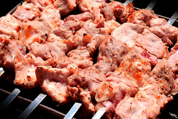 Preparation of shish kebab from marinated meat on skewers. Pieces of pork strung on metal sticks are prepared on hot coals. Close-up. People cook food in the summer.
