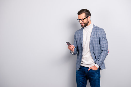 Harsh, virile, modern, attractive man with bristle, hairstyle in jacket and turtleneck  using 3G internet, holding smart phone, hand in pocket, reading sms, email over gray background with copy space