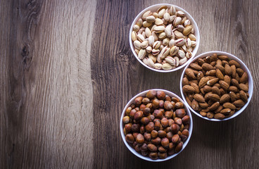 Mixed nuts in a white ceramic bowl on a wooden background.