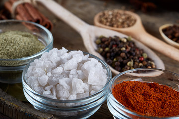 Various spices in wooden spoons and bowls and some salt on an old wooden barrel, top view, close-up, selective focus.