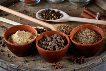 Various spices in wooden spoons and bowls on an old wooden barrel, top view, close-up, selective focus.