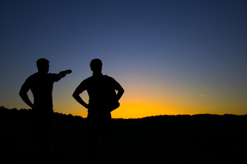 Fototapeta na wymiar Silhouette of two men, One person shows a direction with his hand, against the background of the sunset. Tourism.