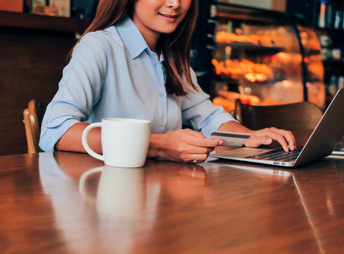 Close up asain woman hands with creadit card and laptop in coffee shop.