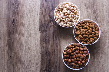 Mixed nuts in a white ceramic bowl on a wooden background.