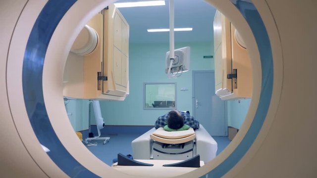 Patient lying on the CT or MRI scanner. Patient's scanning procedure is starting with CAT-scanner's elements launching