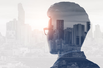 The double exposure image of the business man standing back during sunrise overlay with cityscape...