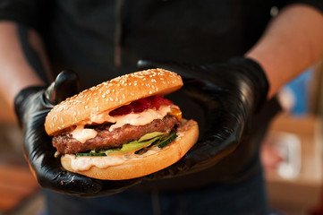 Fresh burger cooked at barbecue outdoors. Burger with meat and vegetables close-up, chef unfocused...