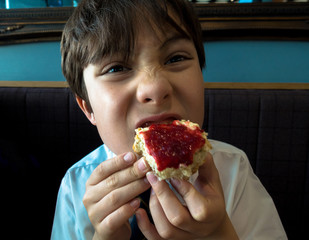 A young boy eating a scone with clotted cream and jam.