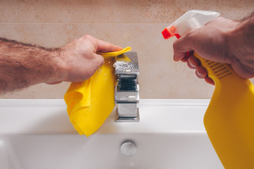 A man sprinkles a detergent on a new chrome bathroom faucet