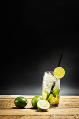 glass of delicious mojito on a wooden table with pieces of lime and mint leaves on a black background