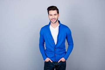 Portrait of good guy in blue cardigan holding his hands in pocket, looking at camera, standing over grey background