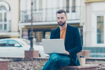 Portrait of busy smart man in jeans jacket sitting outdoor using laptop chacking email chatting with partners having weekend vacation holidays