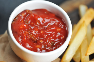 In the frame, a cup of ketchup and French fries. Close-up. Gray background. Macro photography.