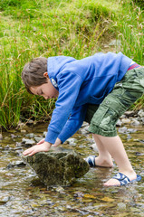 A young boy playing with a rock in a stream.
