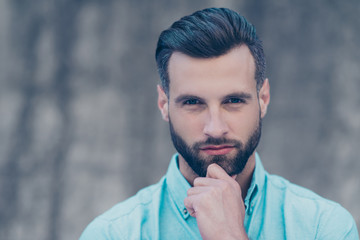 Horizontal portrait with copy space for advertisement of serious clever man with modern hairdo holding hand on chin looking at camera isolated on blurred grey background