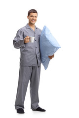 Young man in pajamas holding a pillow and a cup
