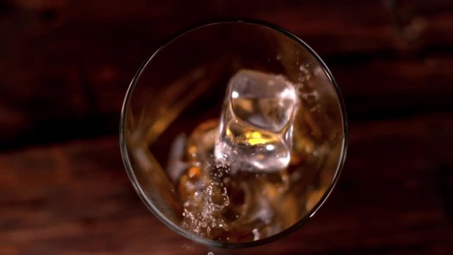 Super slow motion of falling ice cube into whiskey glass, top view. Filmed on cinema slow motion camera, 1000fps