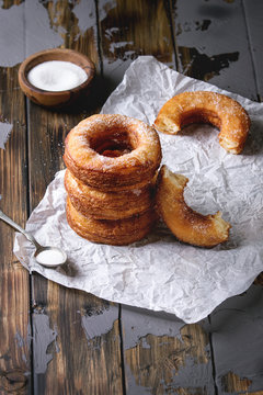 Homemade puff pastry deep fried donuts or cronuts in stack with sugar standing on crumpled paper over dark wooden concrete table.