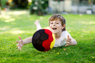 Obraz premium Happy active kid boy playing soccer with ball in German flag colors. Healthy child having fun with football game and action outdoors