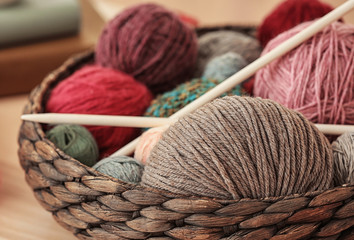 Wicker basket with knitting threads and needles on table, closeup