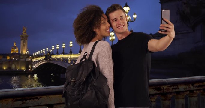Happy and attractive couple take selfie on beautiful night in Paris, Millennial male and female take picture together by the Seine, 4k
